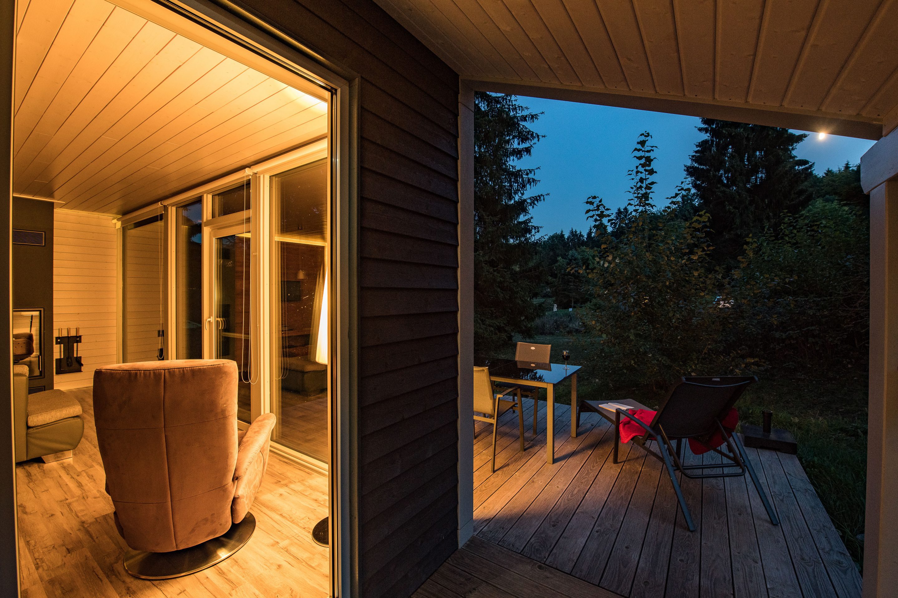 Beleuchteter Innenraum und Terrasse eines modernen Ferienhauses im Herbst bei Abenddämmerung